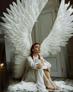 a woman sitting on the floor with large white wings