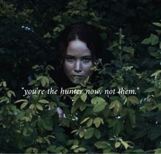 a woman peeking out from behind some trees with the words you're the hunter now not them