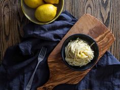 a bowl of spaghetti and lemons on a wooden cutting board next to a blue towel