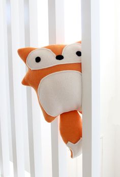 an orange stuffed animal hanging from the side of a crib with white slats