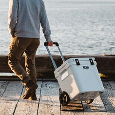 a man pulling a cooler on wheels by the water