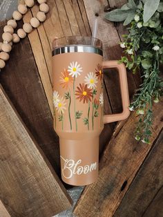 a coffee cup with flowers painted on it and the word bloom written in white lettering