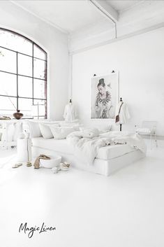 a white room with a large window and lots of pillows on the bed in front of it