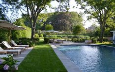 an outdoor pool with lawn chairs and umbrellas next to the swimming pool, surrounded by trees