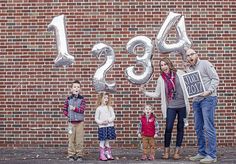 a group of people standing in front of a brick wall holding up large silver balloons