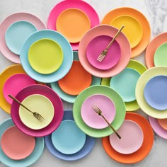 a pile of colorful plates with forks and spoons on top of each one in different colors