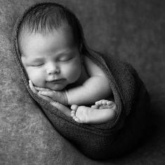 a newborn baby is curled up and sleeping on a gray blanket with his hands under his chin