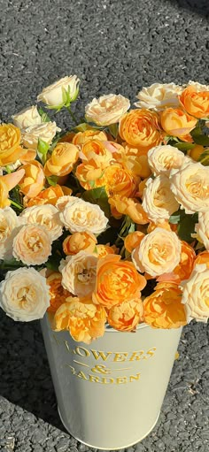 an arrangement of yellow and white roses in a bucket on the ground, with one flower still blooming