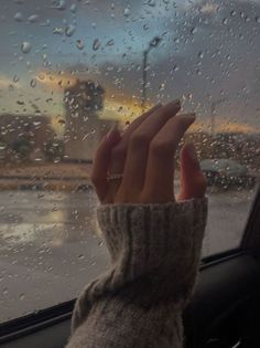 a woman's hand on the windshield of a car, with raindrops