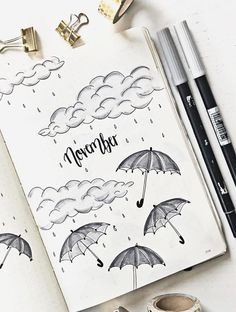 an open notebook with rain and umbrellas on it next to some pens, markers and pencils