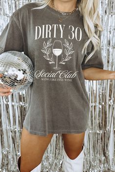 a woman holding a disco ball in front of a tin foil wall with the words dirty 30 on it