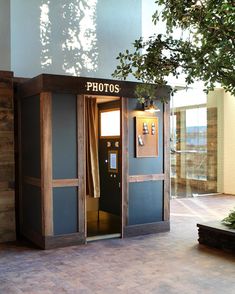 an open phone booth sitting on the side of a building next to a green tree