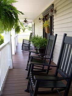 four black rocking chairs sitting on a porch with plants growing out of the top one