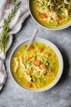 two bowls filled with chicken and rice soup on top of a gray table next to a napkin