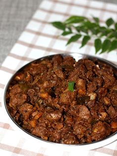 a bowl filled with meat and vegetables on top of a checkered table cloth next to a potted plant