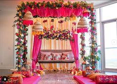 a decorated stage with pink and yellow drapes, flowers and pillows on the floor