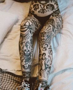 a person with tattoos on their legs and leggings sitting on top of a bed