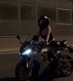 a woman riding on the back of a black motorcycle at night with her helmet on