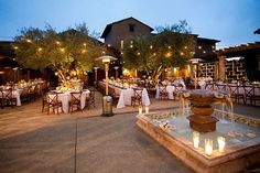 an outdoor dining area is lit up with candles and tables set for dinner at dusk