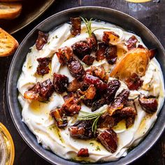 a bowl filled with whipped cream and dried fruit on top of a wooden table next to bread