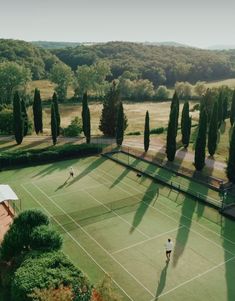 an aerial view of two people playing tennis on a green court with trees in the background