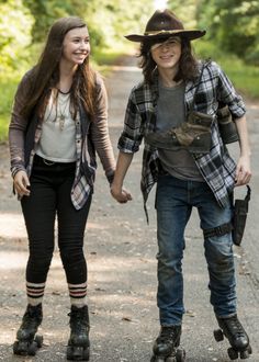 two young women rollerblading down a dirt road holding each other's hands