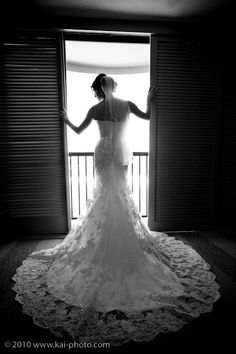 a woman standing in front of a window wearing a wedding dress and holding her arms out