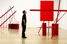 a man standing in front of a red sculpture on top of a hard wood floor