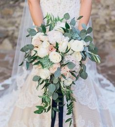 a bridal holding a bouquet of white flowers and greenery in her hands,