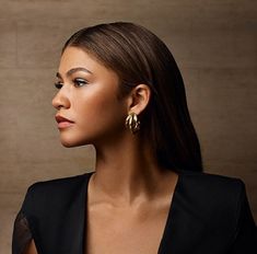 a woman in a black top and gold earrings looking off to the side with her hand on her hip