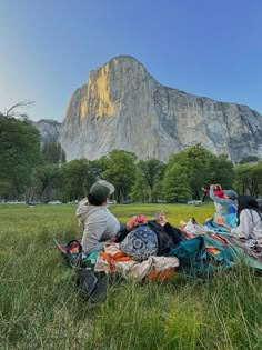 two people sitting on the grass in front of a large mountain with a sky background