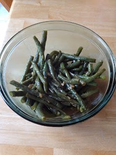 a glass bowl filled with green beans on top of a wooden table