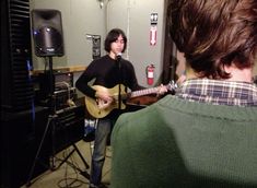 a man playing a guitar in front of a microphone and another person standing next to him