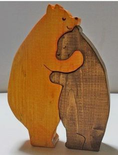 two wooden bears standing next to each other on top of a white surface with one bear hugging the other