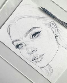 a pencil drawing of a woman's face on paper with a pen next to it