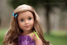 a doll with long blonde hair wearing a purple dress and butterfly clip on her head