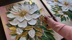 a person is painting flowers on canvases with gold leaf trimmings and metallic foil