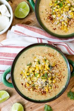 two green bowls filled with soup on top of a wooden table next to limes