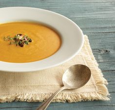 a white bowl filled with carrot soup on top of a table next to a spoon