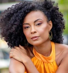 a close up of a person wearing an orange shirt and large earrings with her arms crossed