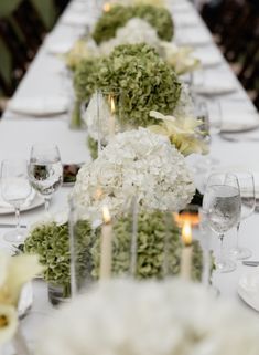 a long table is set with white flowers and candles for an elegant dinner or reception