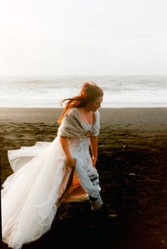 a woman sitting on top of a wooden bench next to the ocean