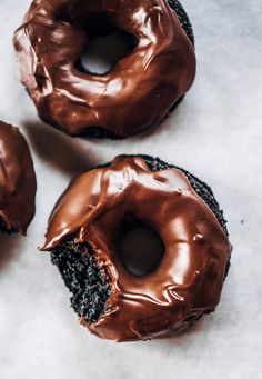 three chocolate doughnuts with frosting and sprinkles sitting on a table