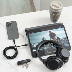 a tablet, headphones and cell phone are on a table next to a coffee cup