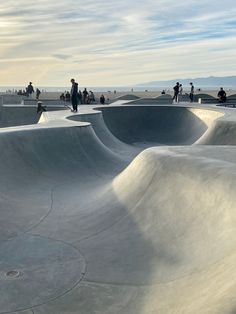 several skateboard ramps with people standing on them and in the background, there is a sky filled with wispy clouds