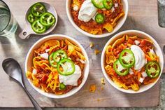 three bowls of chili pasta with sour cream and jalapenos on the side