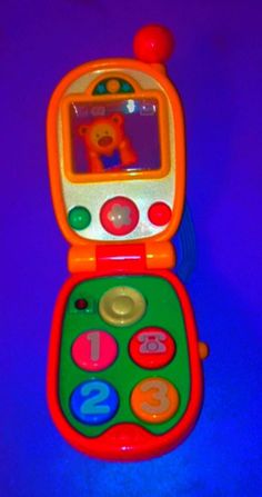 an orange and green toy phone with numbers on it's display stand in front of a purple background