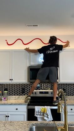 a man standing on top of a kitchen counter next to a sink and stovetop