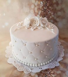 a white cake sitting on top of a table next to a doily covered wall