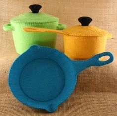 three different colored pots and pans sitting on a tablecloth covered surface with a brown cloth back ground